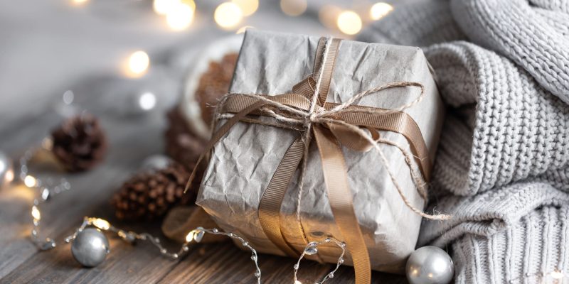 Close-up of a gift box, details of a festive Christmas decor and knitted elements on a blurred background with bokeh.