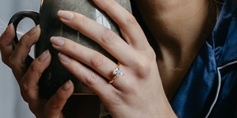 ladies hand wearing a diamond ring holding a coffee cup